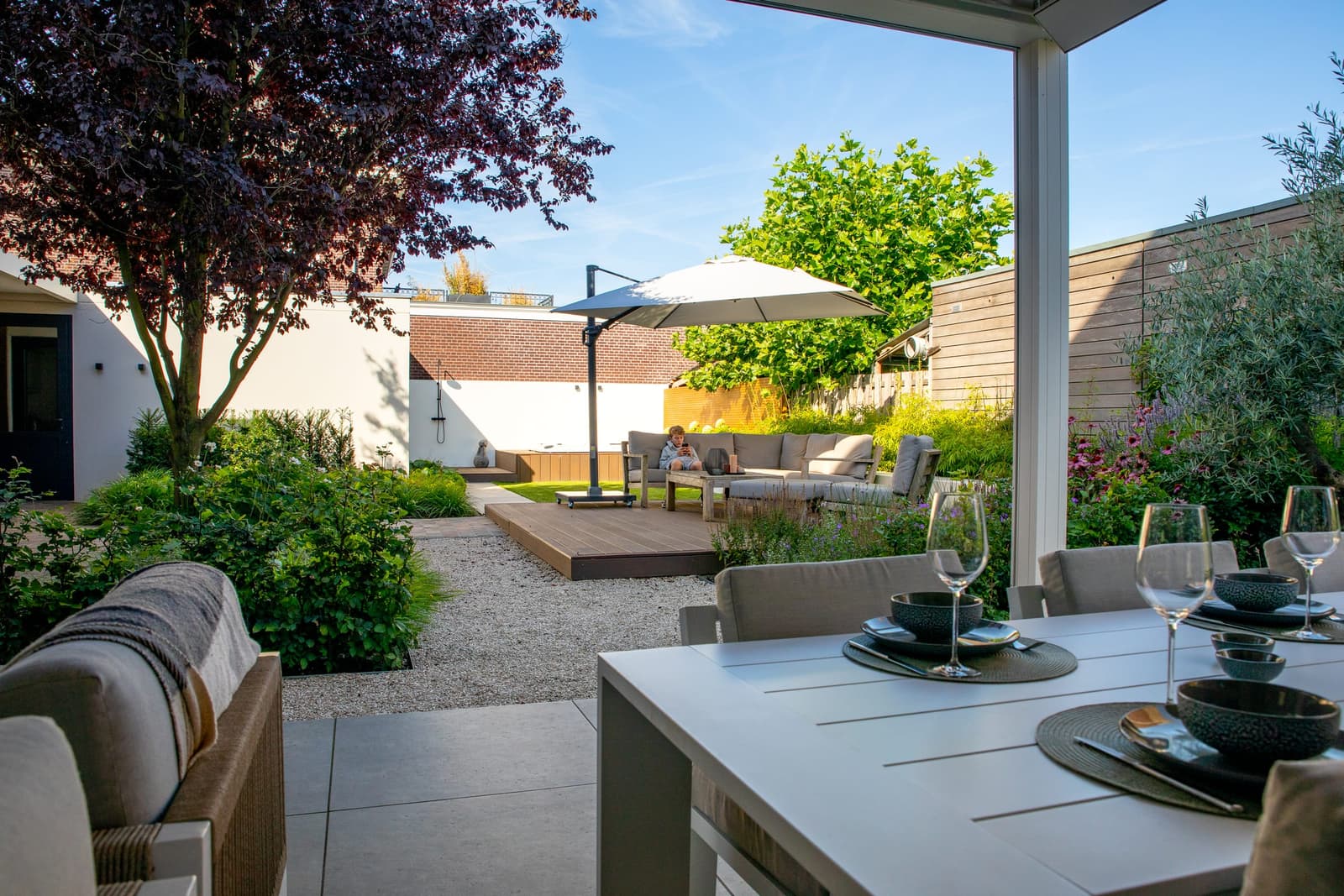 Aangelegde achtertuin met een keramisch terras, houten vlonder met loungeset en borders vol beplanting